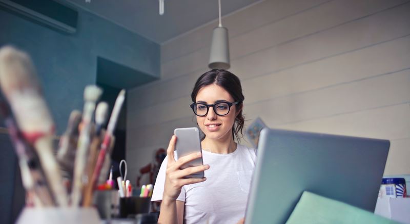 Girl looking at a cell phone and typing on a laptop